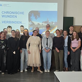 Ein Gruppenfoto mit allen Teilnehmenden des Seminar, vor einer Leinwand, welche die Folie zeigt "Chronische Wunden...verbinden..."