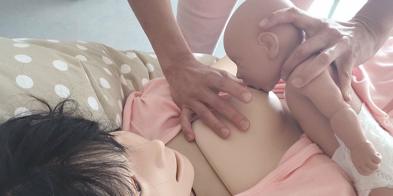 eine Studierende hilft einer Mutter (Puppe) beim Stillen ihres Babys (Puppe)