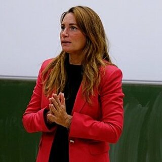 Eine Frau im roten Blazer steht in einem Hörsaal.