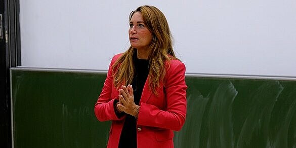 Eine Frau im roten Blazer steht in einem Hörsaal.