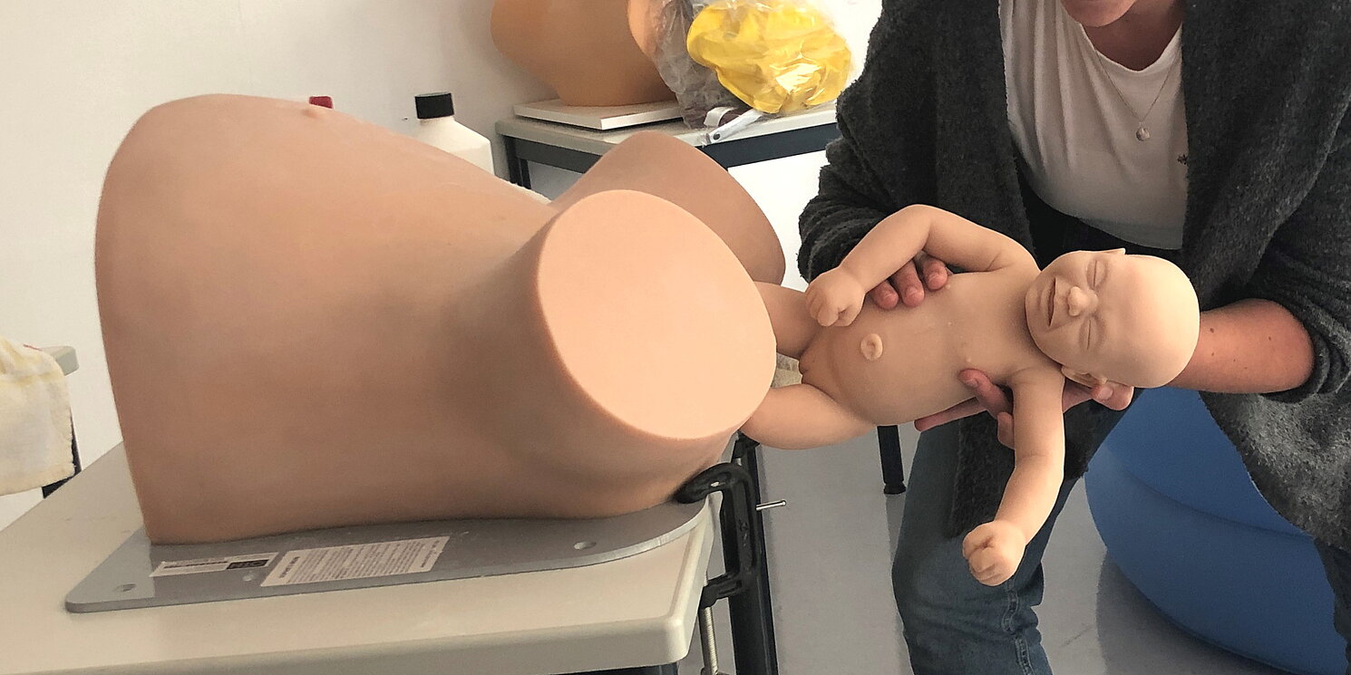 eine Studierende hält das Modell eines Neugeborenen beim Austritt aus dem geburtshilflichen Phantom