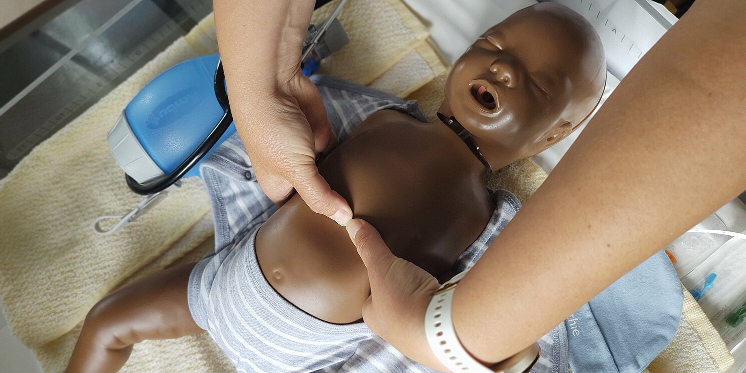 An einer Babypuppe wird die Herzdruckmassage im Rahmen des Reanimationstrainings gezeigt.