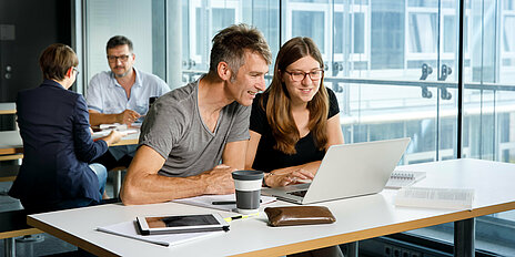 Vier Studierende lernen und arbeiten an ihren Tischen mit Büchern und Laptops
